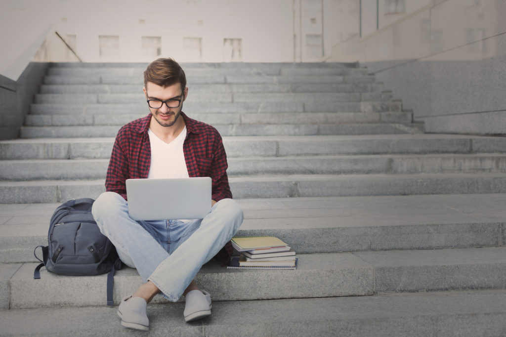 Smiling communication sciences and disorders student sitting on stairs working with laptop